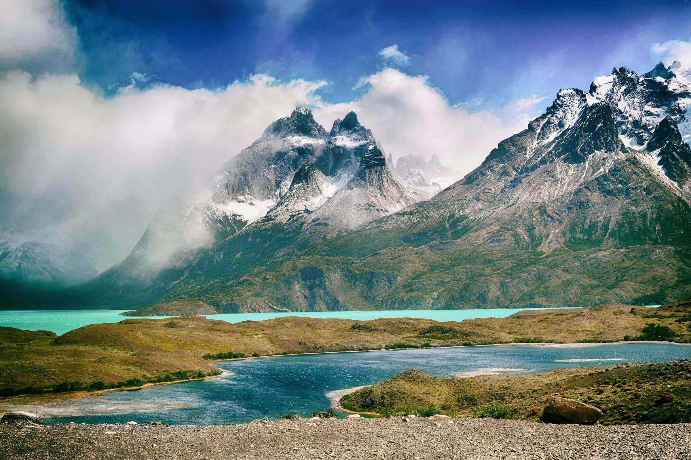 Cloud-wreathed peaks of Torres del Paine above a turquoise lake and golden steppe