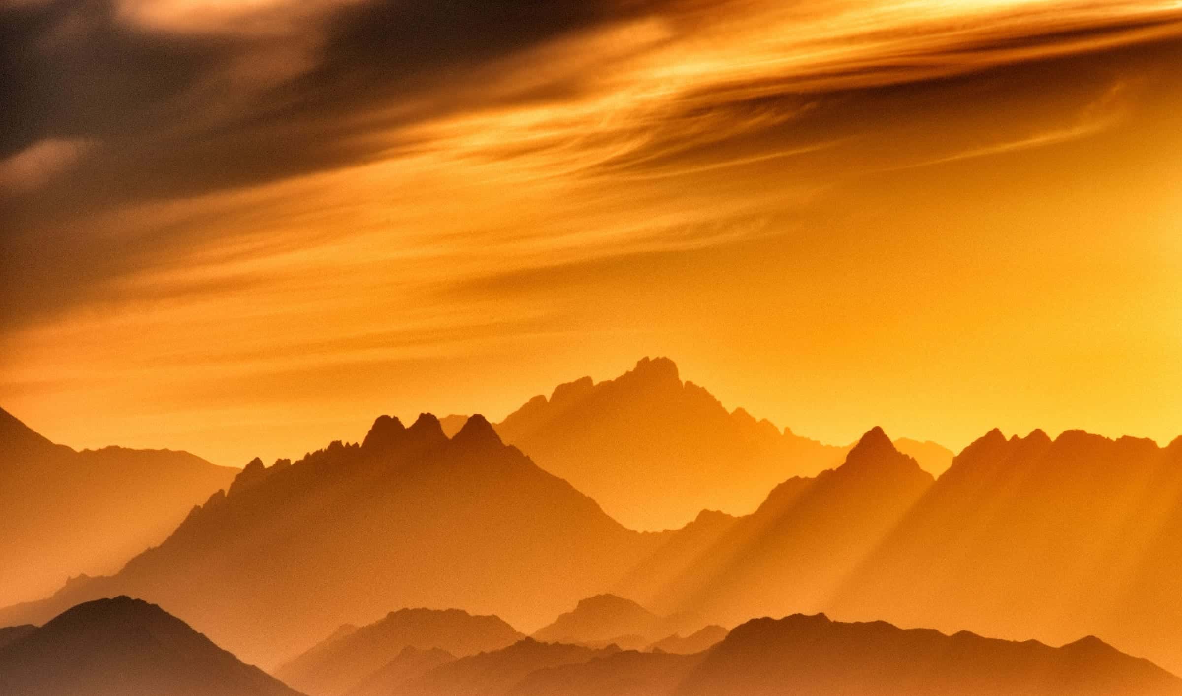 Layered mountain ridges in golden haze, with sun rays falling through evening cloud