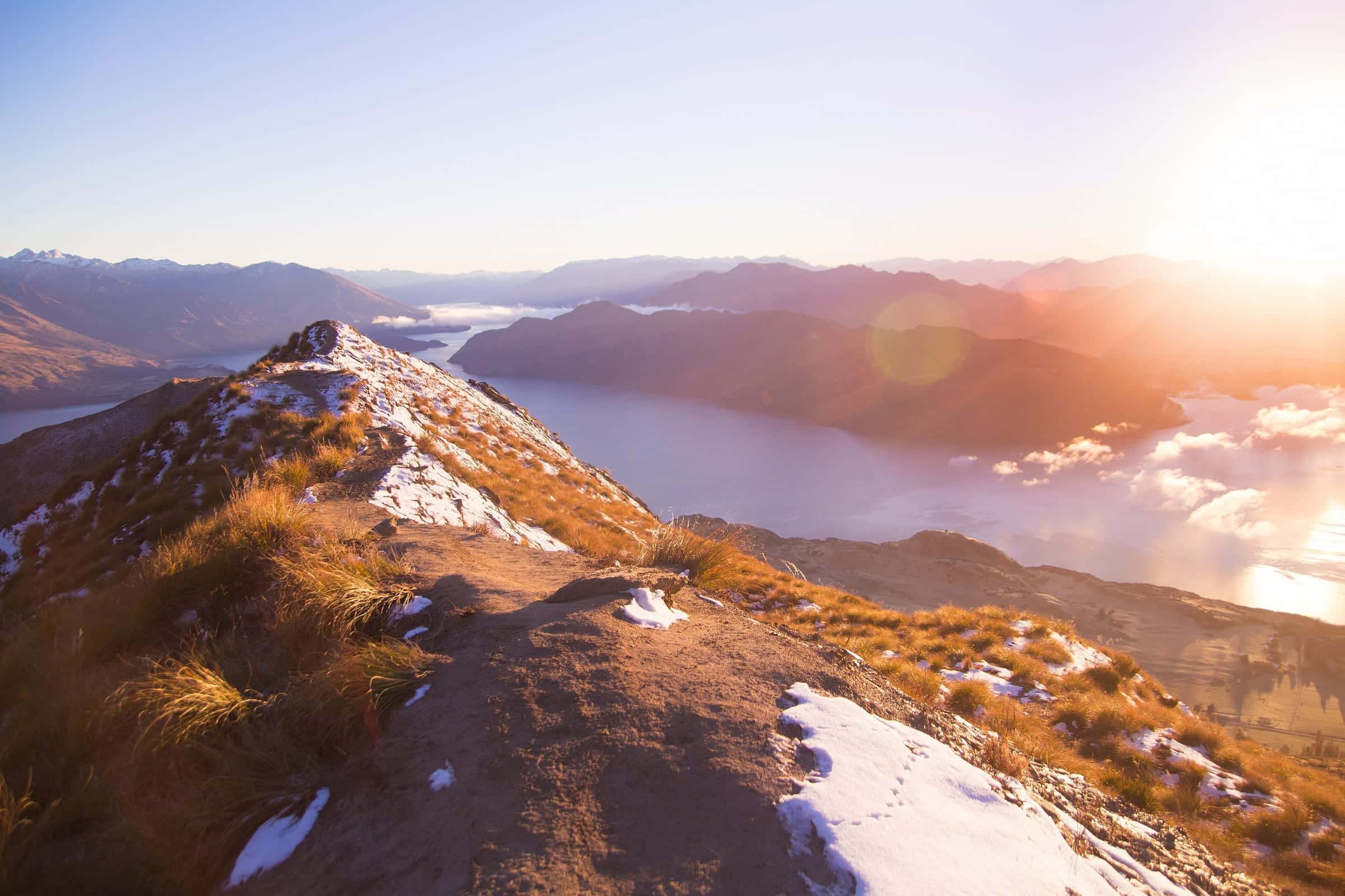 A golden, snow-dusted ridge rising toward a blazing sunrise over a lake and cloud
