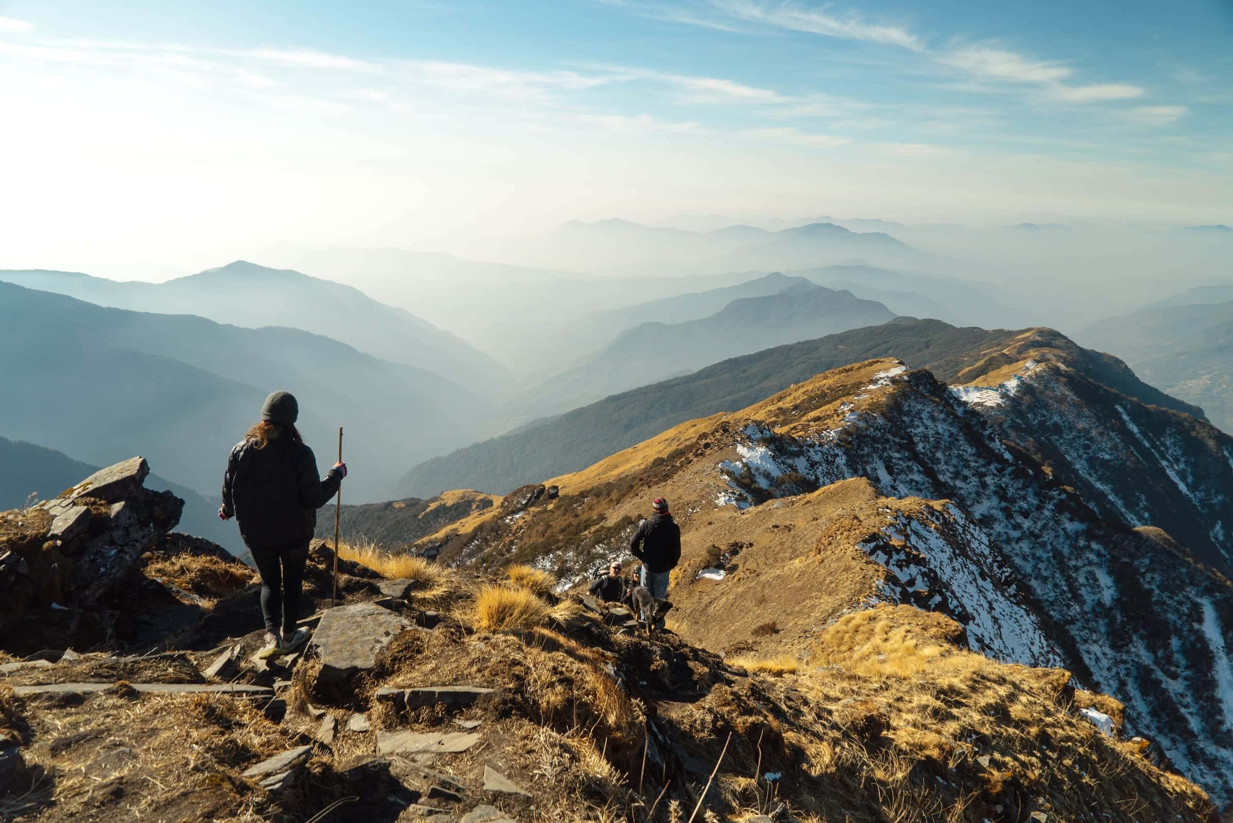 Two hikers, seen from behind, descending a rugged golden ridge into hazy blue valleys