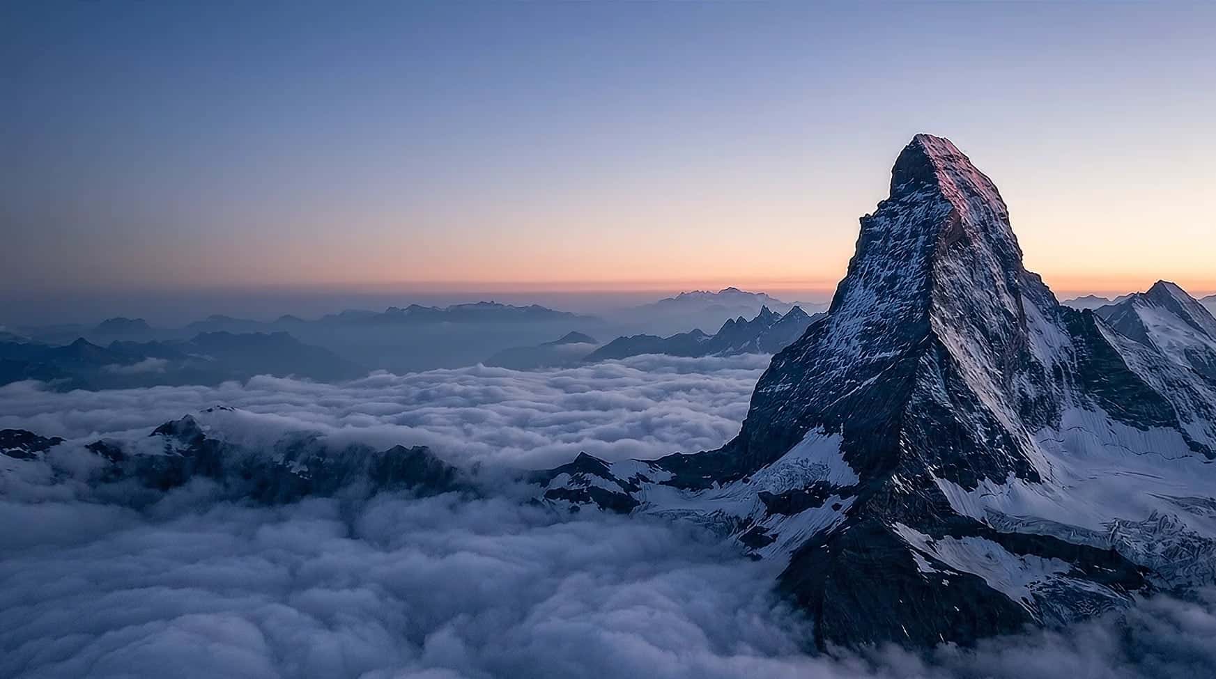 The Matterhorn before dawn, rising out of a sea of cloud under an indigo sky with a thin peach horizon